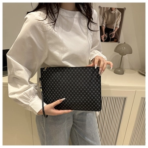 Détail de la pochette noire à carreaux avec fermeture éclair dorée et dragonne amovible
