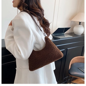 Sac bandoulière en peluche marron en forme de demi-lune porté par un mannequin en costume