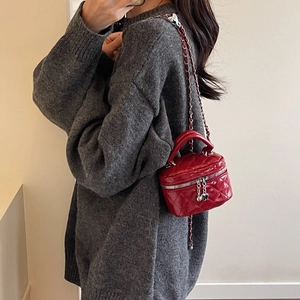 Détail d'un mini sac matelassé rouge avec chaîne et pendentif cœur porté en bandoulière