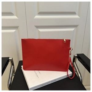 Détail d'une pochette en cuir rouge avec fermeture éclair dorée et dragonne sur un livre