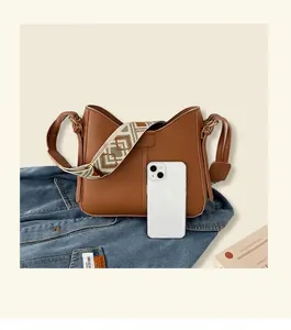 Caramel brown bucket bag with ethnic woven strap next to iPhone for size reference