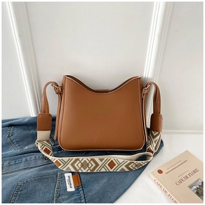 Détail du sac seau en cuir marron avec une large bandoulière tissée géométrique
