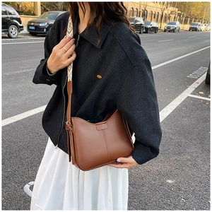 Brown leather crossbody bag featuring a wide ethnic geometric patterned strap in urban setting