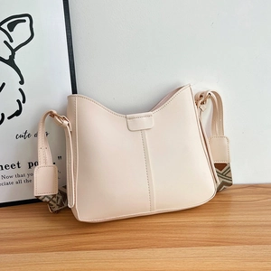 Detail of beige bucket bag with geometric wide strap on a wooden surface