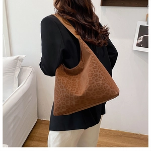 Detail view of a large brown leopard print tote bag worn on shoulder in a home setting
