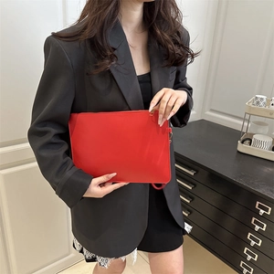 Minimalist red envelope clutch bag with gold zipper and wrist strap carried by a model