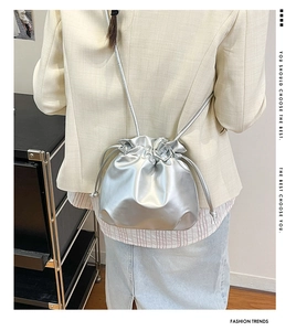 Fashionable silver metallic drawstring bucket bag shown worn on a beige blazer back view