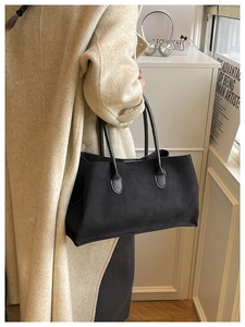 Close-up of black matte tote bag with slim leather handles worn over a beige wool coat