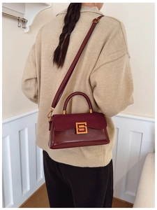 Detail of burgundy crossbody bag with suede flap and gold square geometric buckle