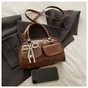 Detail of a brown PU leather crossbody bag with pearl bow charm on a grey suit jacket