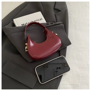 Detail of glossy wine red patent leather crescent bag with golden hardware on a blazer