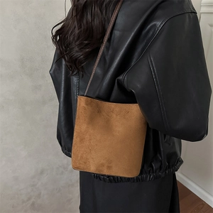 Brown matte suede bucket bag with slim leather strap worn by a model in black leather jacket