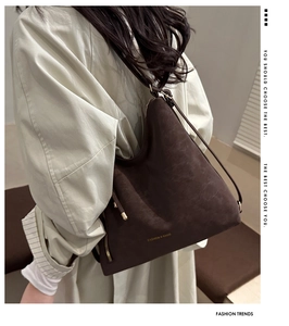 Close-up of a large dark brown matte tote bag with gold lettering on a stylish trench coat