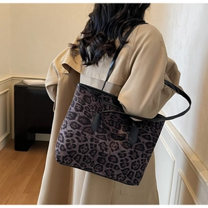 Rear view of a large leopard print tote bag with black leather straps on a beige trench coat