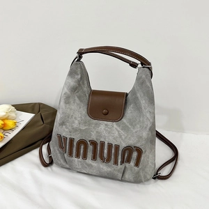 Detail of grey canvas tote bag featuring brown leather trim and intricate embroidery