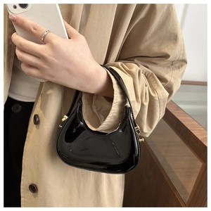 Mini black patent leather dumpling bag with gold hardware held by a fashion model
