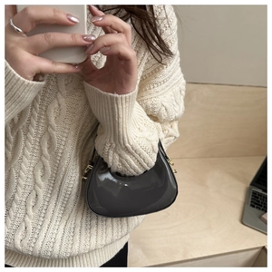 Dark grey patent leather crescent moon bag shown with a beige knit sweater style