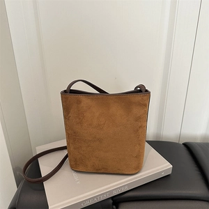 Detail of a brown suede bucket bag with leather strap placed on a vintage book