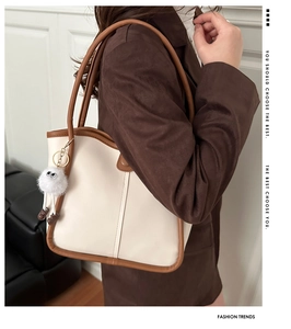Side view of cream and brown tote bag with plush charm on model in minimalist interior