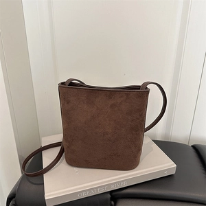 Detail view of dark brown suede bucket bag with slim shoulder strap on a book
