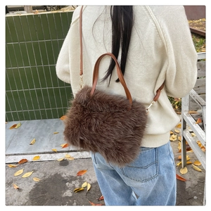 Close-up of brown faux fur handbag with leather strap on person in outdoor autumn setting
