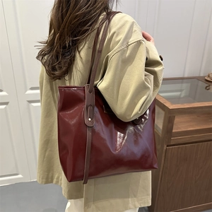 Sac fourre-tout rouge foncé brillant avec anses brunes porté sur un trench beige