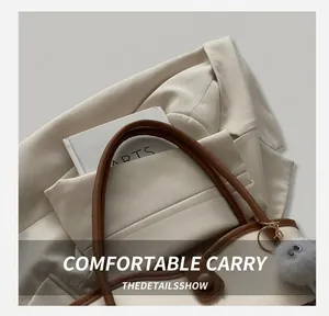 Detail of cream tote bag with brown handles, plush charm and metal ring fasteners