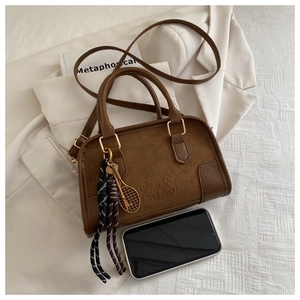 Detail of brown suede retro handbag featuring embossed logo and tennis racket pendant decoration