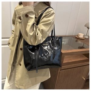 Detail of glossy black faux leather tote bag showing fashion tag and elegant shoulder strap