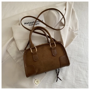 Detail of a brown suede and leather pillow bag placed on a cream blazer for a chic look