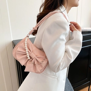 Sac rose à nœud avec poignée en perles et bandoulière porté par un mannequin en blazer
