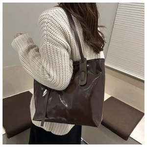 Detail of dark brown patent leather tote bag showing glossy texture and side strap accents