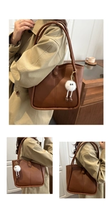 Brown leather tote bag detail with plush charm and side view in cozy indoor setting