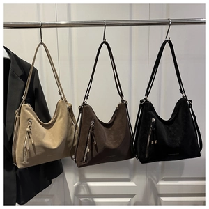 Détail de trois sacs hobo en daim mat kaki, marron et noir suspendus sur un support