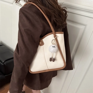 Large beige tote bag with dark brown leather trim and cute monster plush pendant