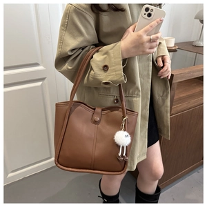 Detail of dark brown matte leather bucket bag with a cute white plush monster keychain