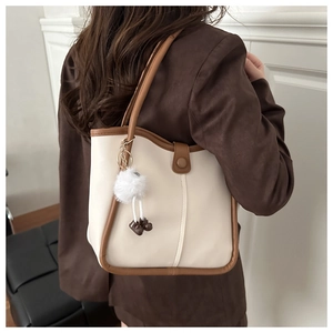 Détail d'un sac seau bicolore avec breloque en peluche et longue bandoulière d'épaule