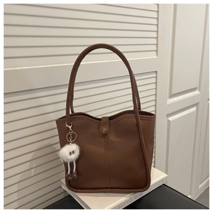 Detail of brown faux leather tote bag with long straps and white plush monster charm