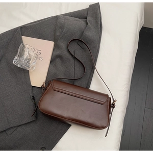 Detailed view of dark brown leather baguette bag with gold metal buckle and exterior pocket