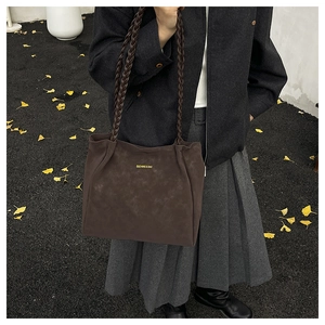 Dunkelbraune Wildleder-Tote Bag mit geflochtenen Griffen auf herbstlichem Hintergrund