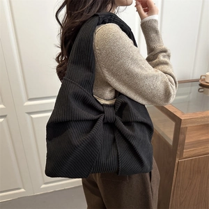 Black corduroy tote bag with large bow design shown on model shoulder for autumn fashion
