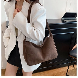 Detail of dark brown suede hobo bag with metal zipper worn with a white blazer