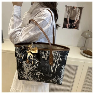 Detail of black tote bag with white bamboo print and brown leather handles and scarf