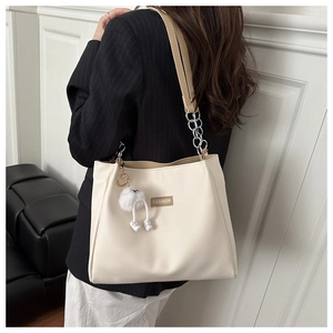 Detail of cream tote bag featuring silver chain strap, leather logo and plush toy charm