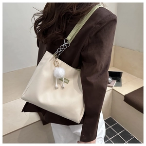 Detail view of beige tote bag with light green chain strap and fuzzy pom pom charm