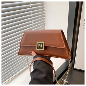 Detail view of brown faux leather handbag featuring a golden M-letter buckle and chain