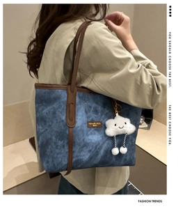 Detail of blue denim tote bag with leather trim and white cloud plush charm accessory