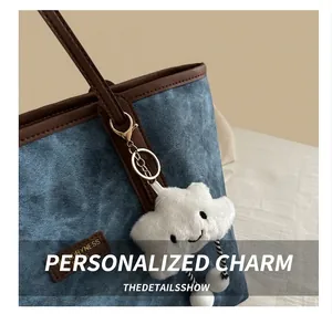 Detail of blue denim tote bag with brown leather trim and white cloud plush charm