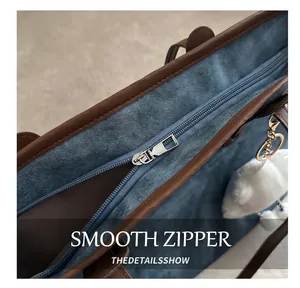 Close-up of smooth metal zipper and brown leather trim on blue denim tote bag