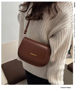 Brown leather saddle bag with gold Fashion text detail shown on beige sweater